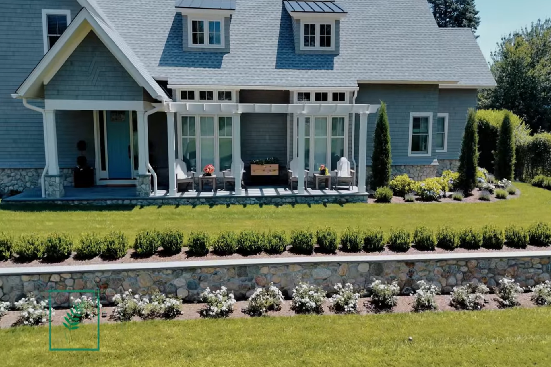 Fieldstone retaining wall with tiered landscaping and planted garden beds in front of a coastal-style Connecticut home.