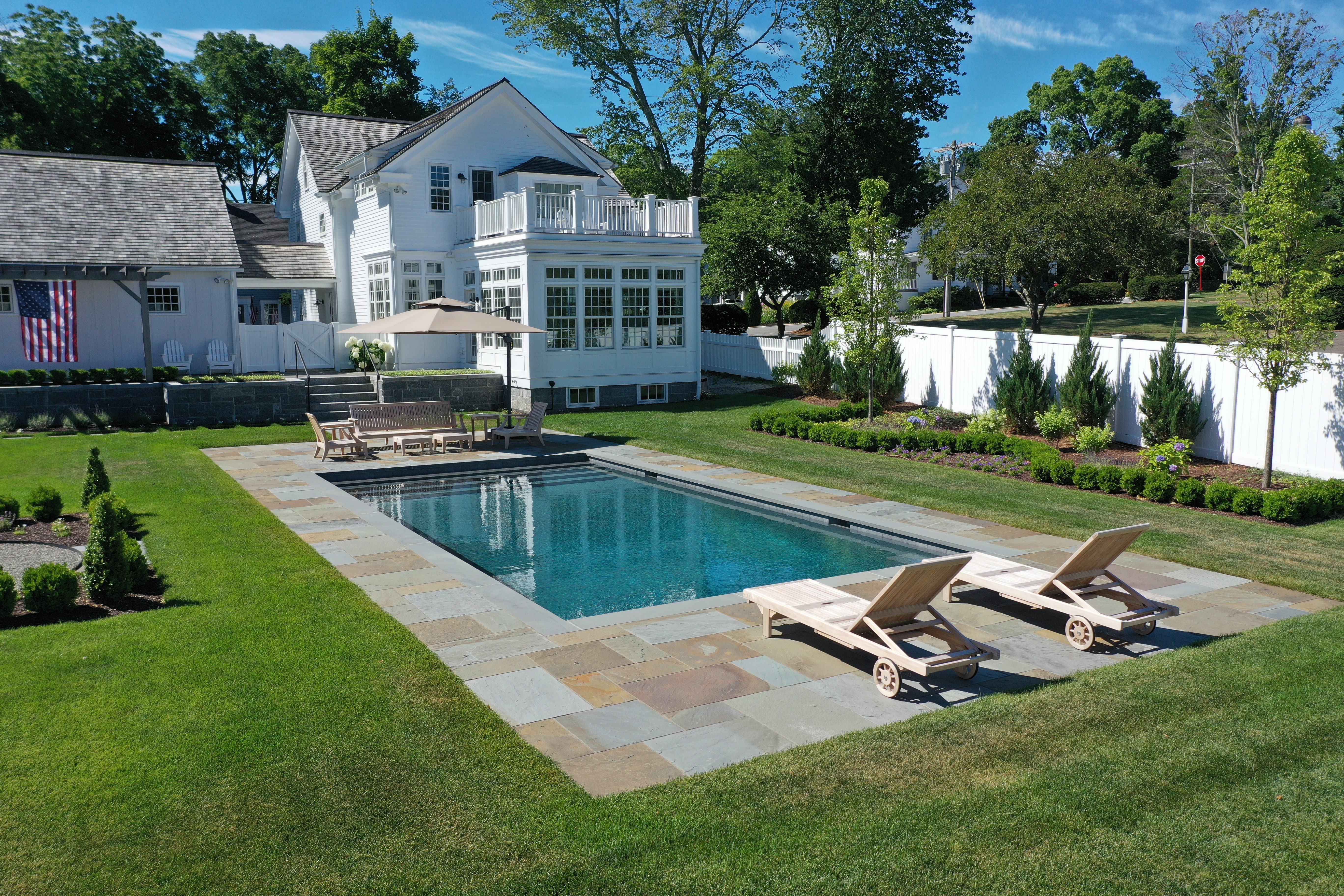 An image of a patio space created by Torrison Stone & Garden that features a pillar-style heater and a fire pit to make the space more comfortable and enjoyable into the fall months and year-round. There are shade umbrellas, tables, an outdoor eating area